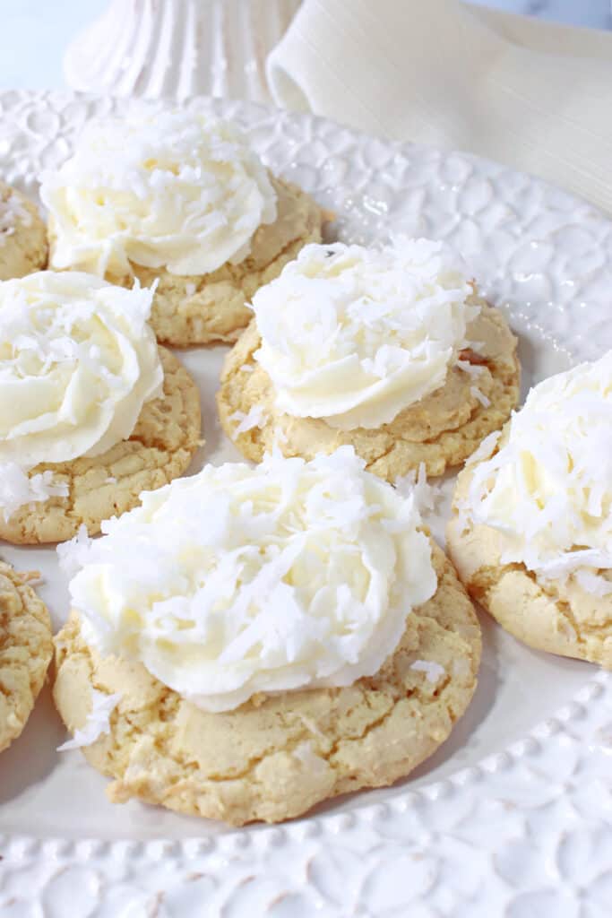 A vertical overhead closeup of a white plate filled with Coconut Cake Cookies with Coconut Buttercream Frosting.