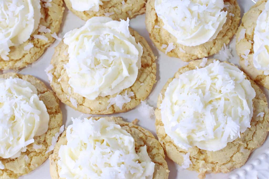 An overhead closeup of coconut topped Coconut Cake Cookies with white Coconut Buttercream frosting.