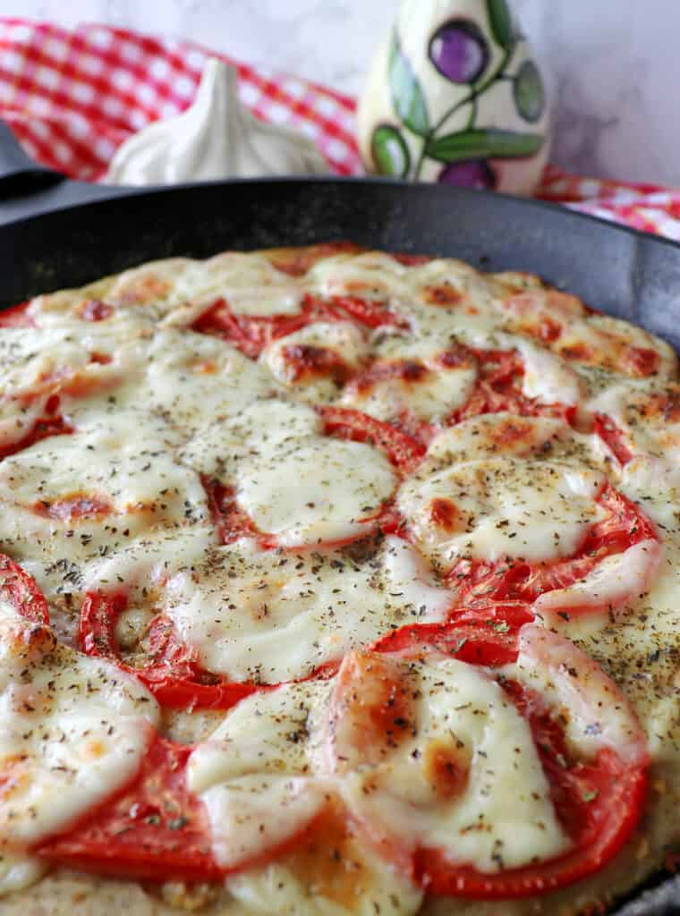 A Deep Dish Garlic Lovers Pizza made in a cast iron skillet with a red and white checkered napkin in the background.