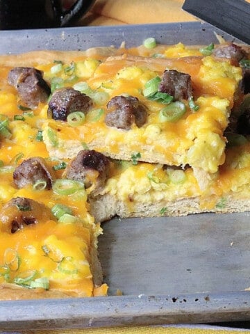 A baking sheet with a Scrambled Egg Breakfast Pizza with a slice taken out.