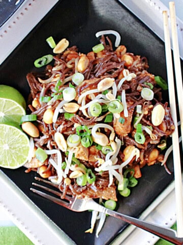 A square black plate filled with a serving of chicken pad Thai with peanuts, limes and bean sprouts.