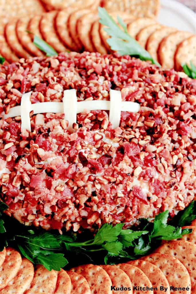 A vertical overhead closeup of a Football Shaped Cheeseball with bacon and pecans on the outside along with string cheese laces.