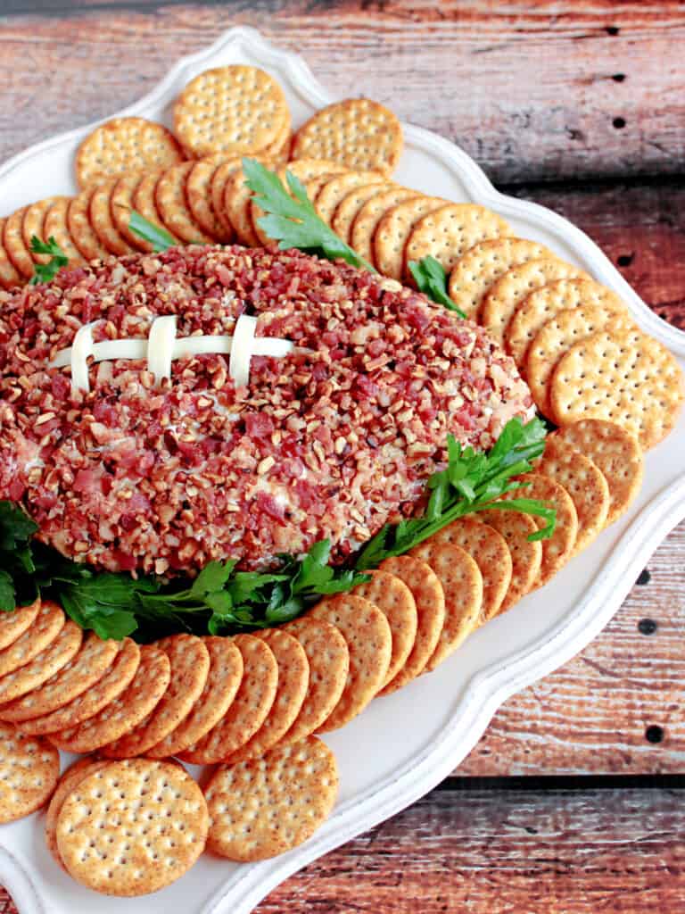 A vertical closeup of a Football Shaped Cheeseball with string cheese laces and pecan and bacon "leather."