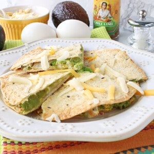 Triangles of an Grated Egg Avocado Quesadillas on a plate with a colorful napkin underneath and some avocados and eggs in the background.