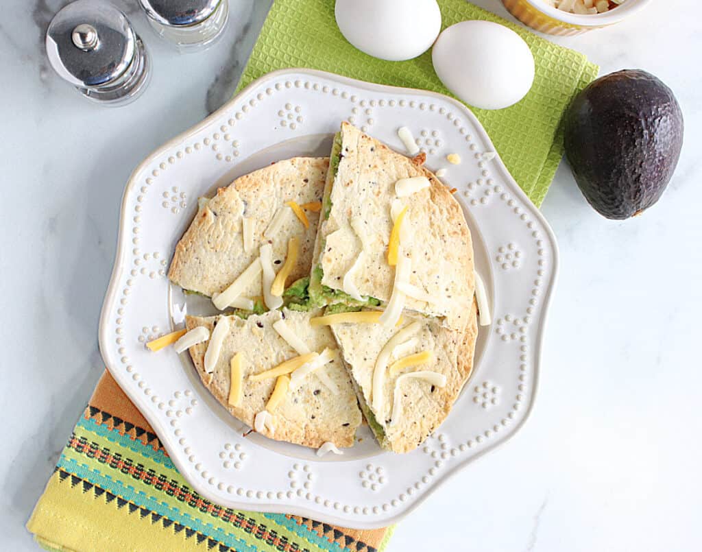 An overhead photo of wedges of a Grated Egg Avocado Quesadilla on a plate with a colorful green napkin underneath.