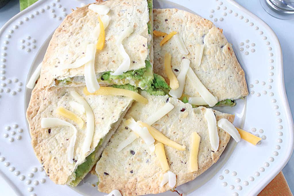 An overhead closeup photo of wedges of a Grated Egg Avocado Quesadilla on a white plate.