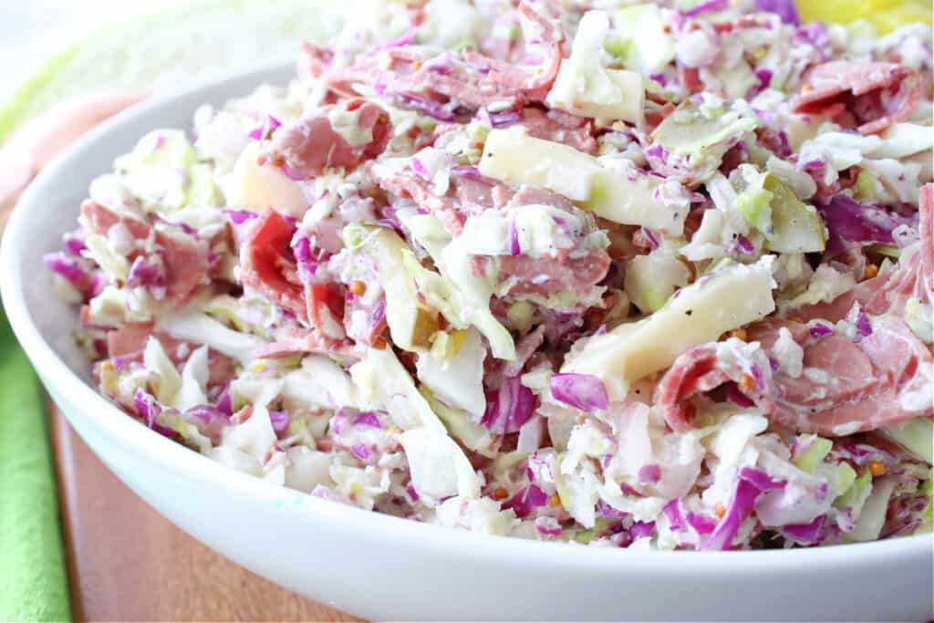A horizontal offset photo of a big bowl of Corned Beef and Cabbage Coleslaw with red cabbage, green cabbage, Swiss cheese and a creamy dressing.