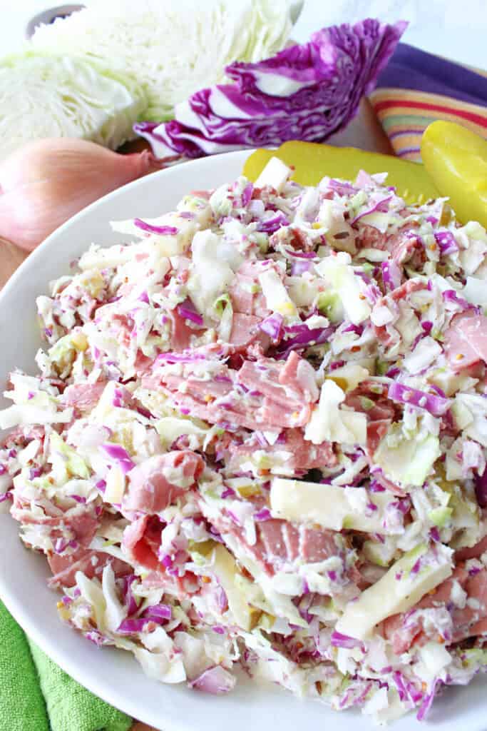 A vertical overhead closeup of a Corned Beef and Cabbage Coleslaw recipe in a white bowl with red cabbage and Swiss cheese.