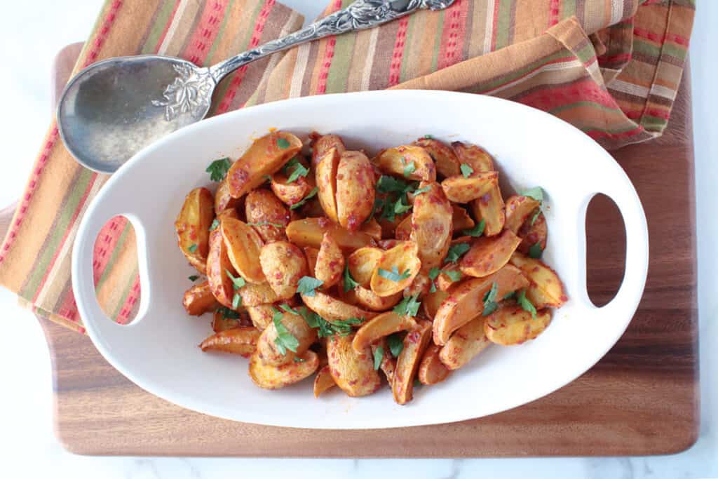 A direct overhead photo of an oval white bowl filled with Roasted Baby Potatoes with Chili Garlic Paste, parsley, and a serving spoon.