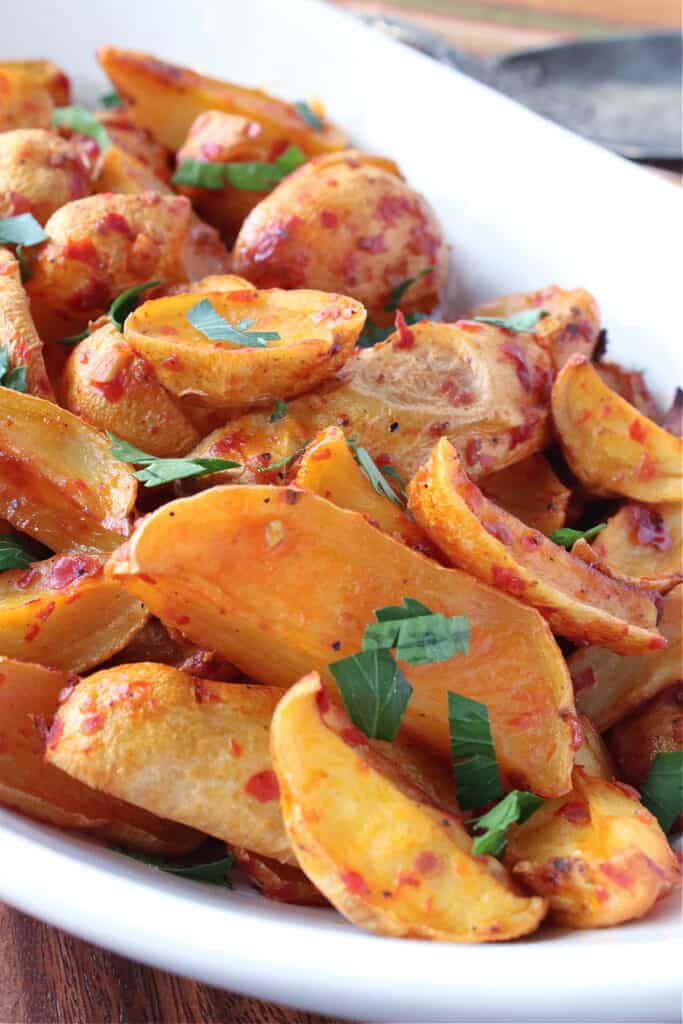 A vertical closeup of a white bowl filled with Roasted Baby Potatoes with Chili Garlic Paste and topped with chopped parsley.