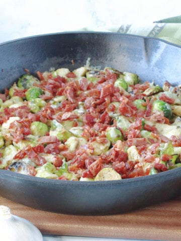 A cast iron skillet filled with Sautéed Brussels Sprouts with Crispy Prosciutto and some green napkins on the side.