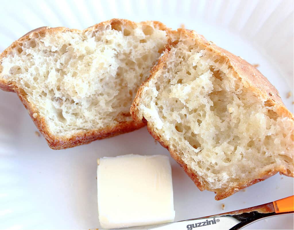 The inside of a Sesame Seed Dinner Roll on a plate with a butter knife and a pat of butter.