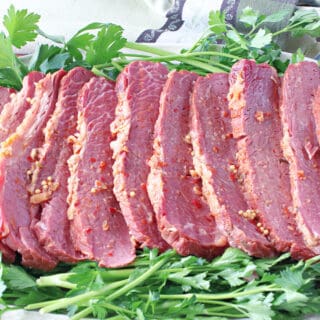 A platter of sliced Slow Cooker Corned Beef with lots of green parsley as a garnish.