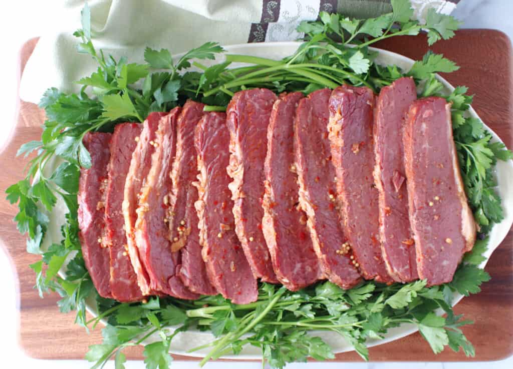 A direct overhead photo of an oval platter filled with sliced Slow Cooker Corned Beef and surrounded by fresh, flat leaf parsley.