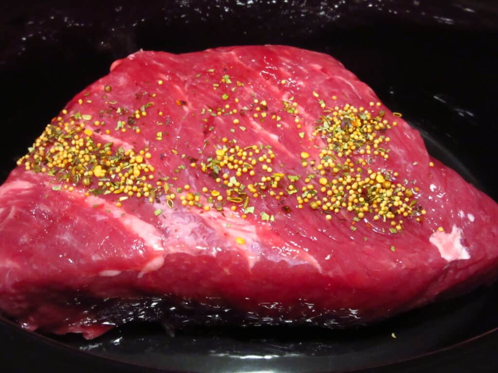 A raw corned beef in a slow cooker with spices.