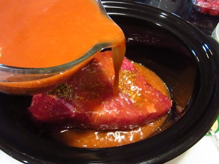 A red pickling spice being poured over a corned beef in a slow cooker.