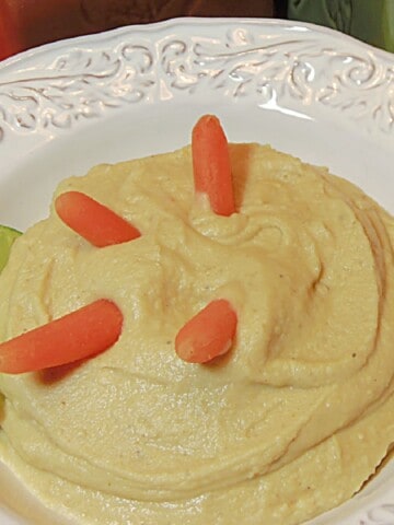 A few carrot sticks in a bowl of White Bean and Artichoke Hummus along with a lime slice.