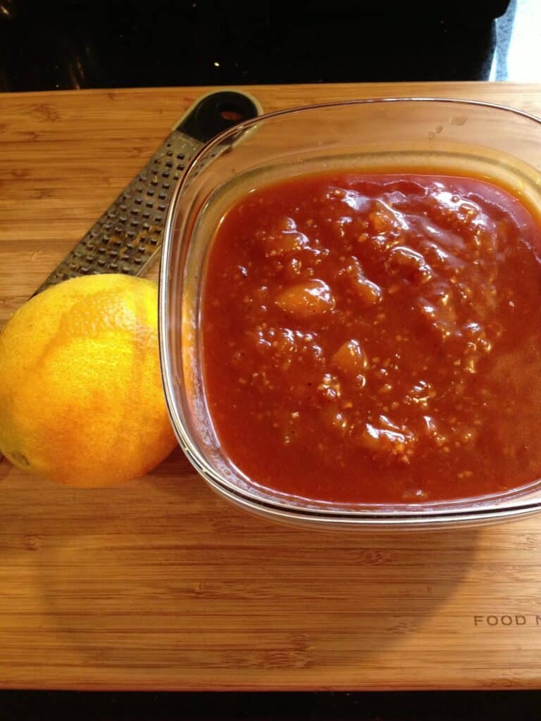 A glass bowl filled with Peach BBQ Sauce with an orange next to it.