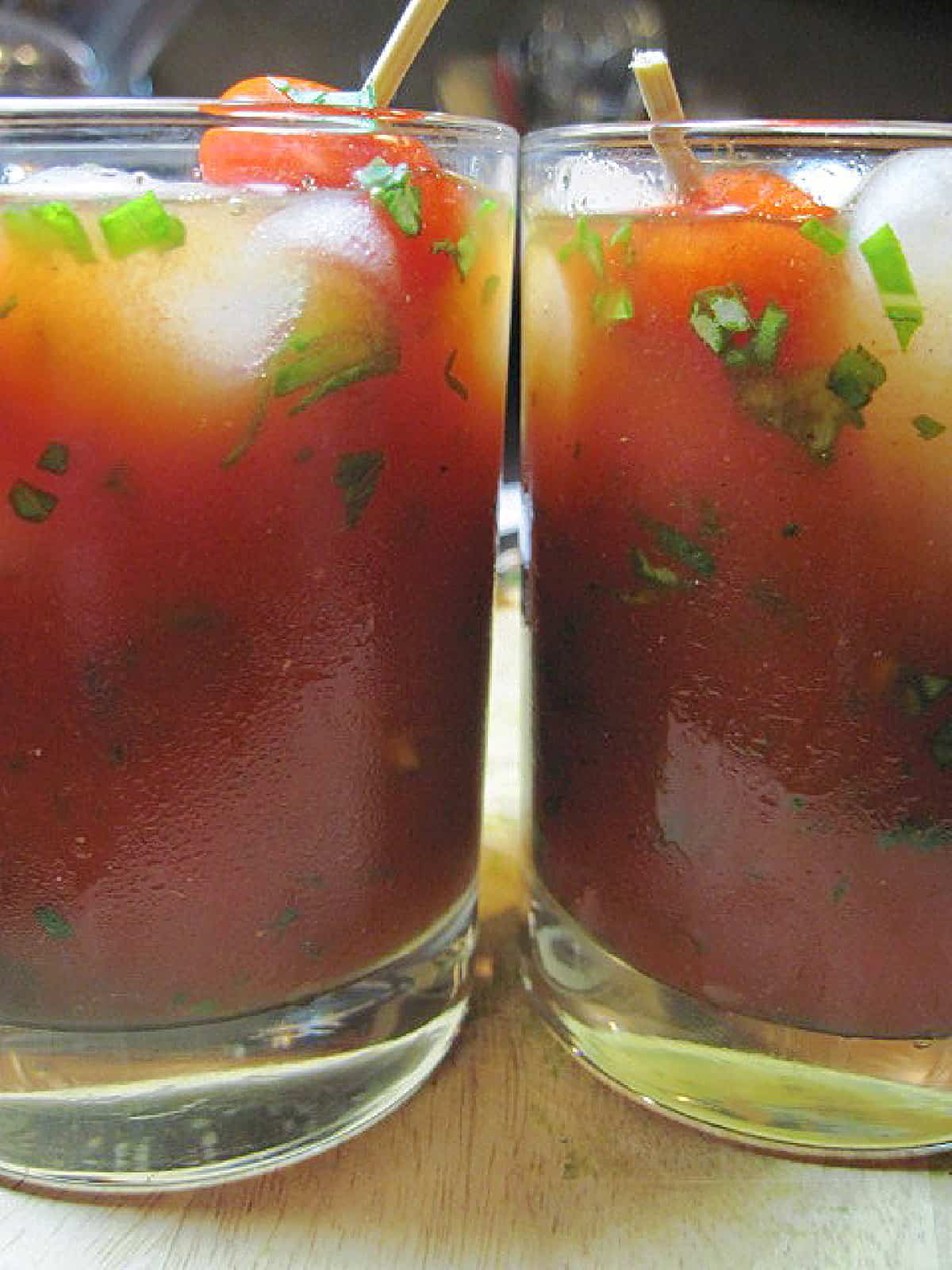 A closeup of two Italian Caprese Cocktails in glasses with ice and chopped basil.