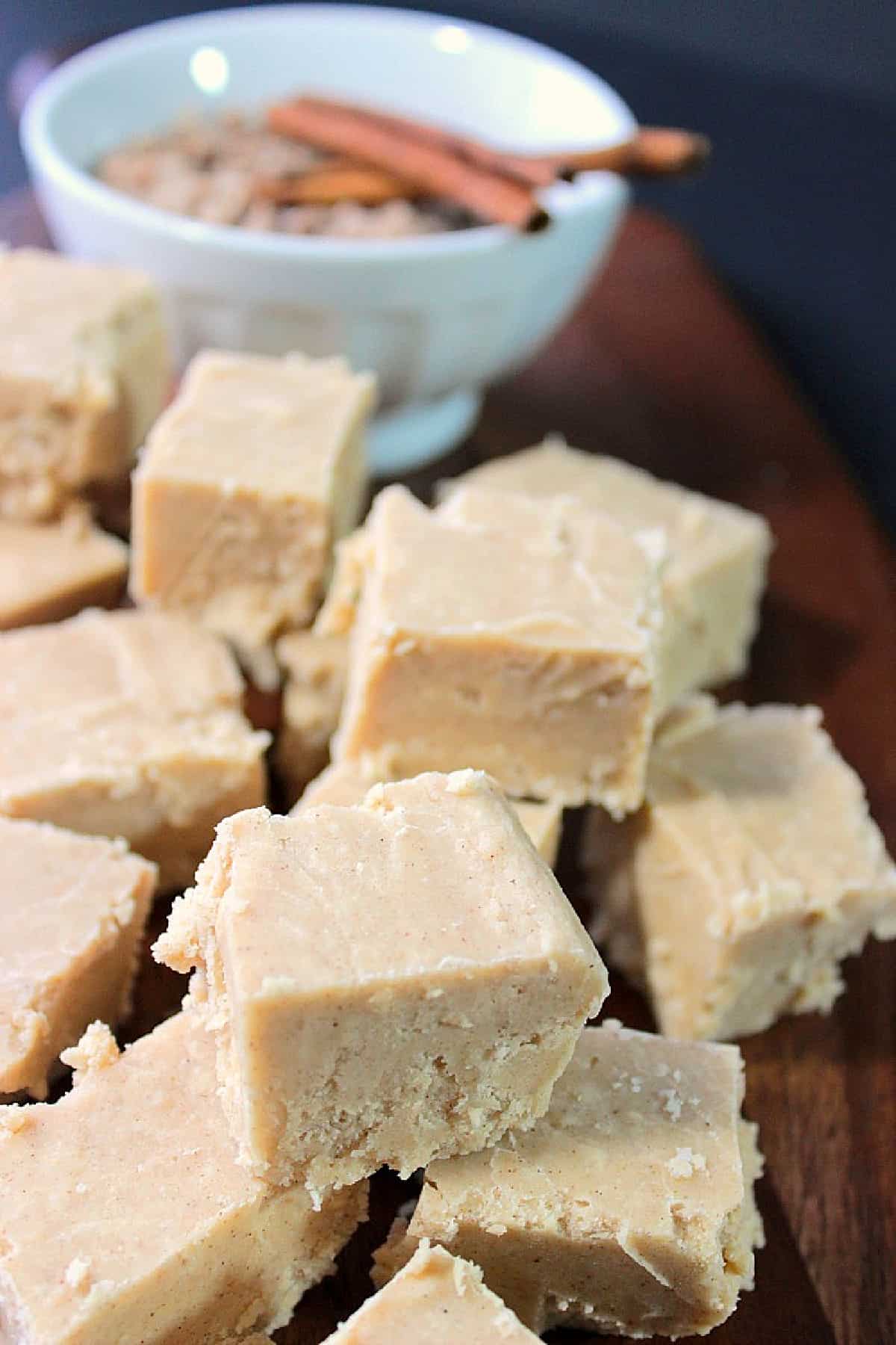 A closeup photo of a stack of Cinnamon Fudge in the foreground and some cinnamon sticks in the background.