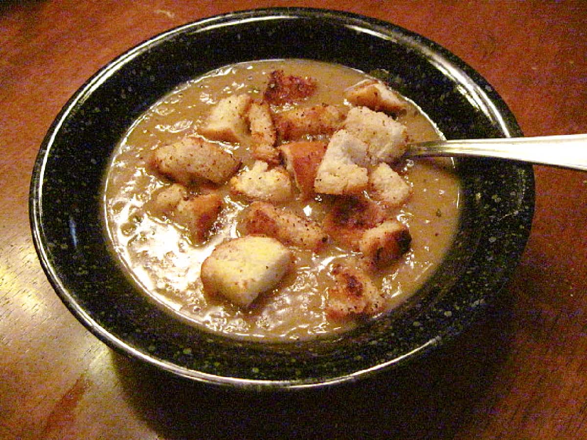 A black bowl filled with a serving of French Onion Lentil Soup with homemade croutons on top.