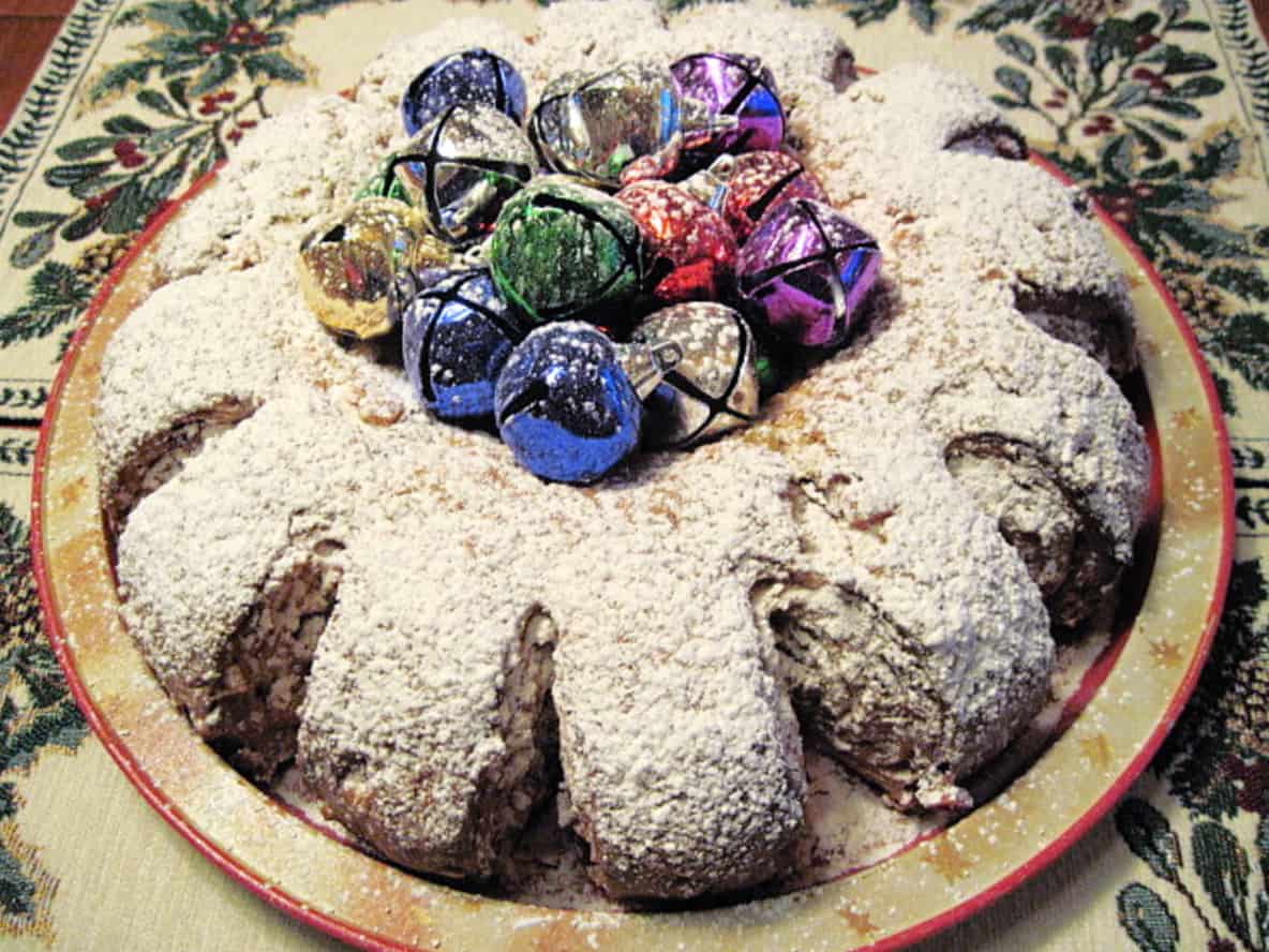 A traditional German Stollen decorated with multi colored bells and powdered sugar on top.