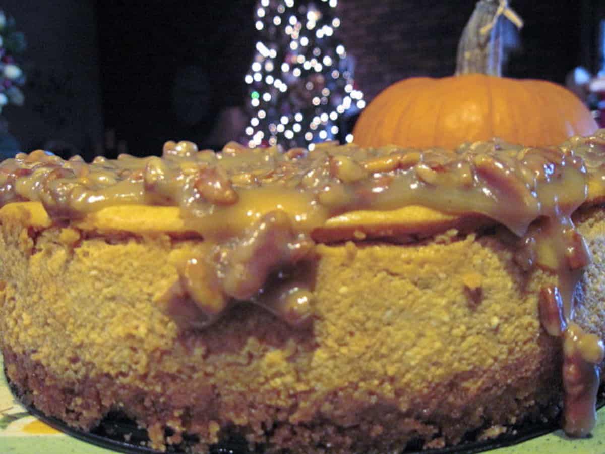 A closeup side view of a Maple Pumpkin Cheesecake with a pumpkin in the background.