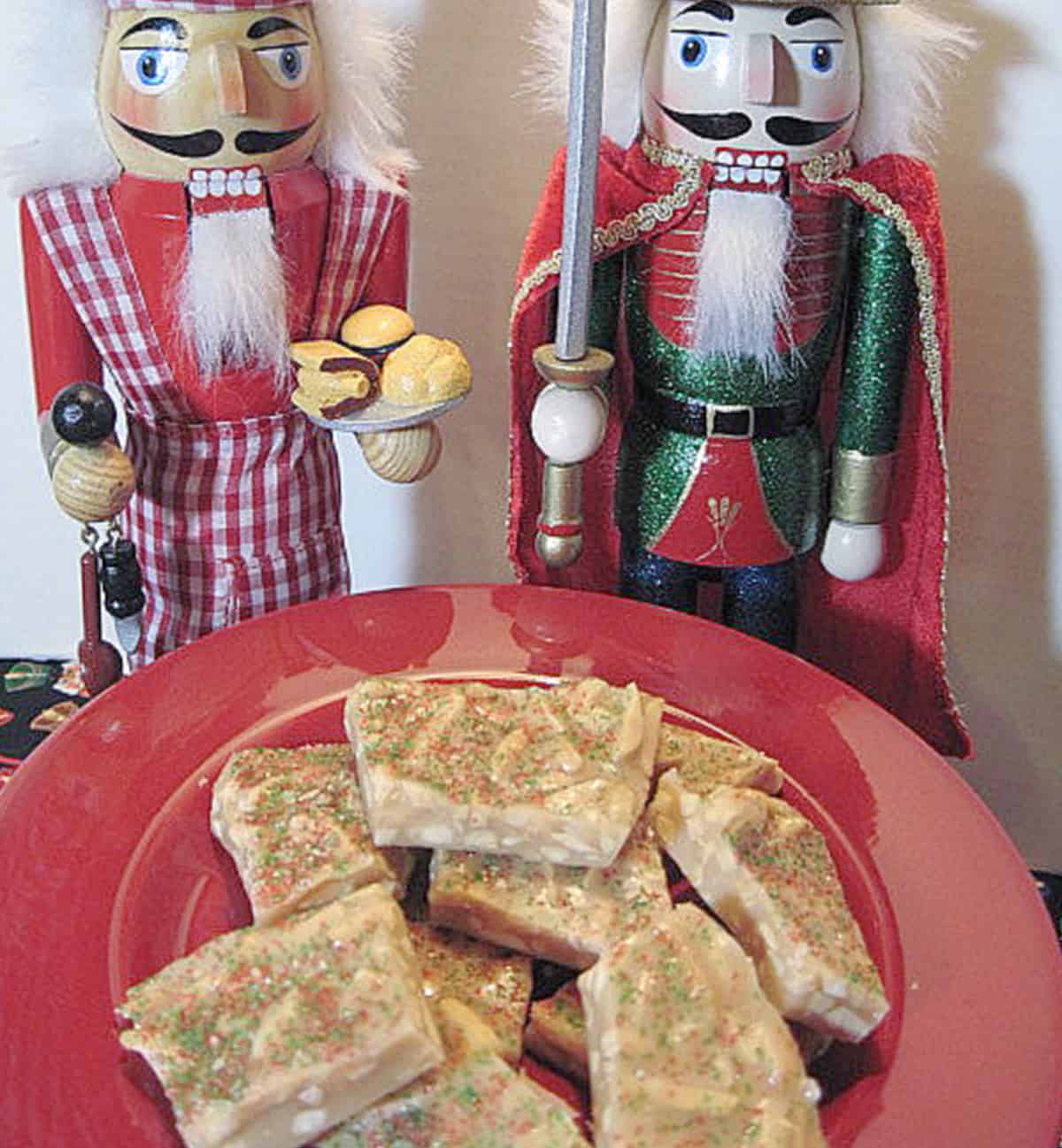 Two nutcrackers standing behind a plate of Almond Butter Crunch Candy.