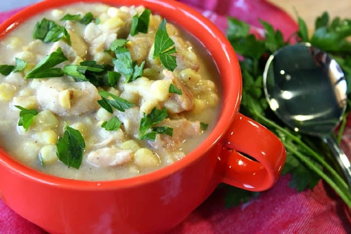 A red mug filled with Chicken Corn Chowder with Bacon and a parsley garnish.