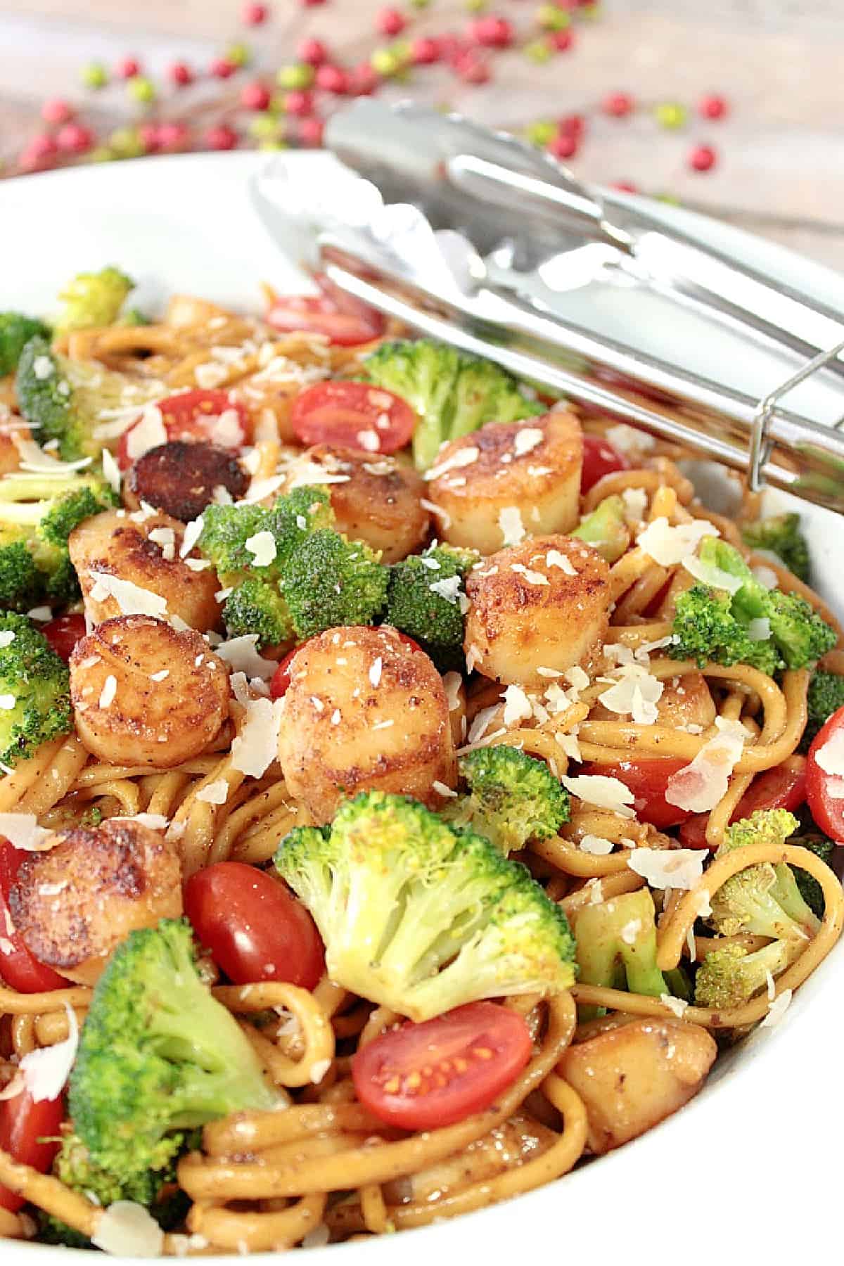 A large white bowl filled with Linguine with Caramelized Scallops and Broccoli along with grape tomatoes and Parmesan cheese.