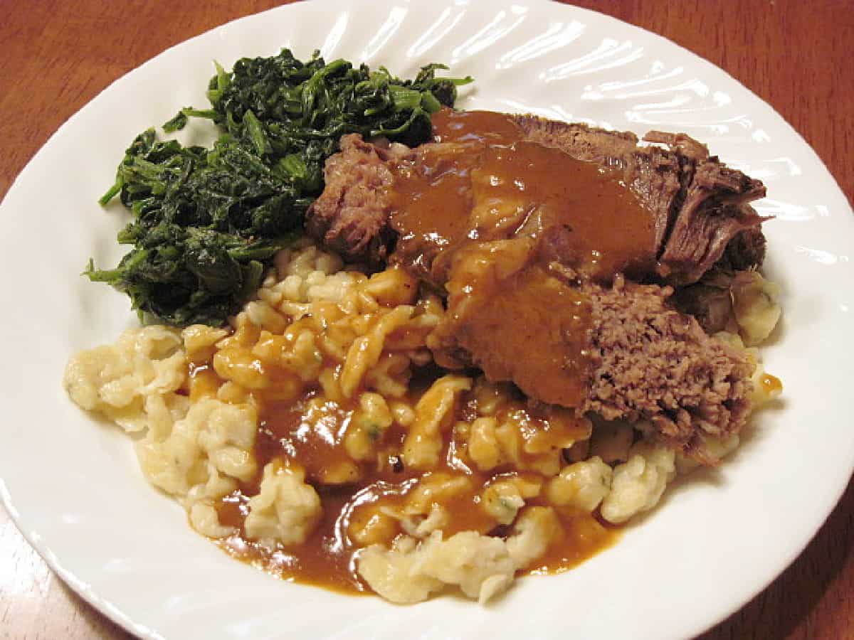 A white dinner plate filled with a serving of Slow Cooker Sauerbraten and thyme spatzle.