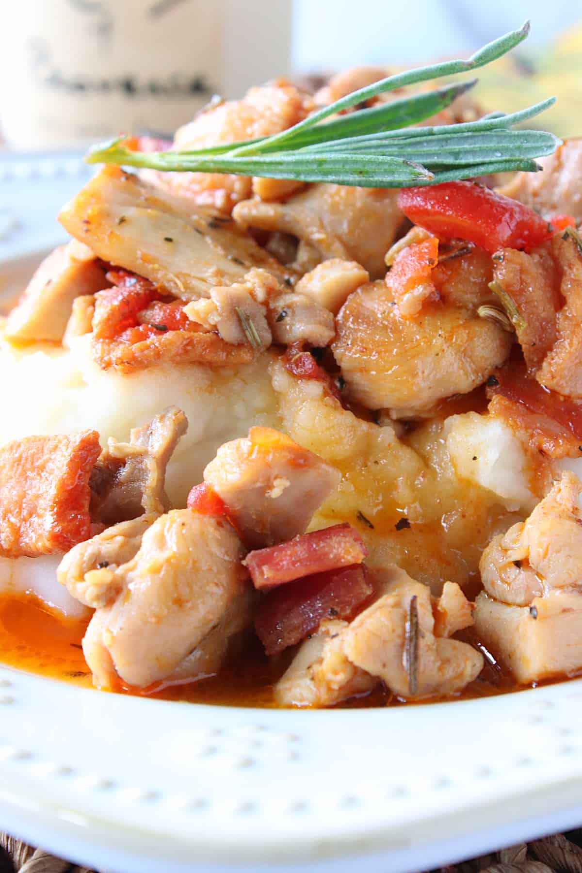 A closeup photo of French Country Chicken over mashed potatoes with gravy, tomatoes, and bacon.