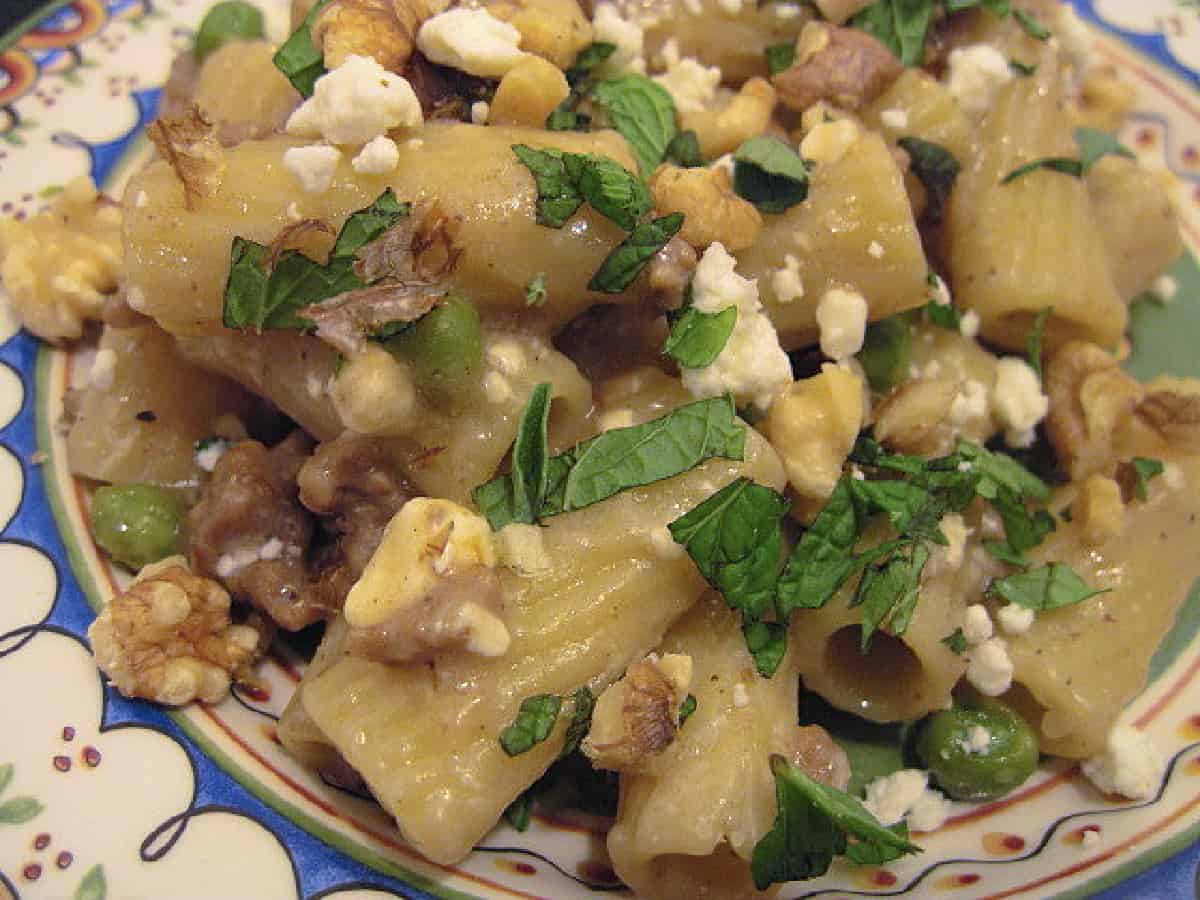 An overhead closeup photo of a serving of Greek Pasta with Lamb and chopped mint along with feta cheese and walnuts.
