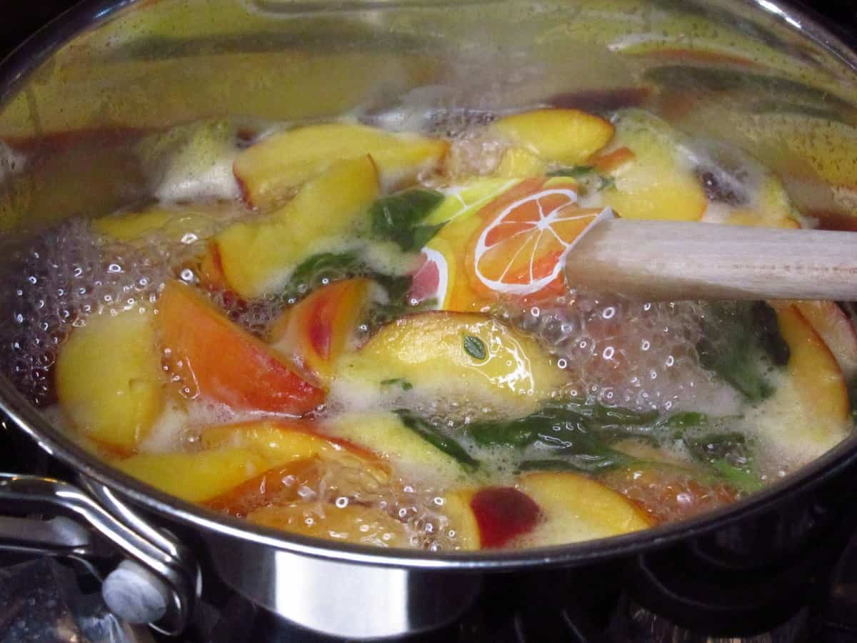 A bubbling mixture of peaches and basil in a saucepan.