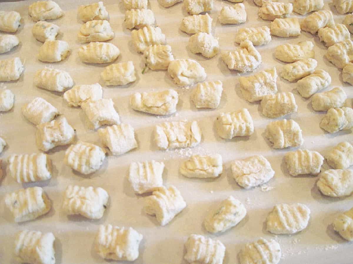 Homemade Ricotta Gnocchi lined up on a floured baking sheet.