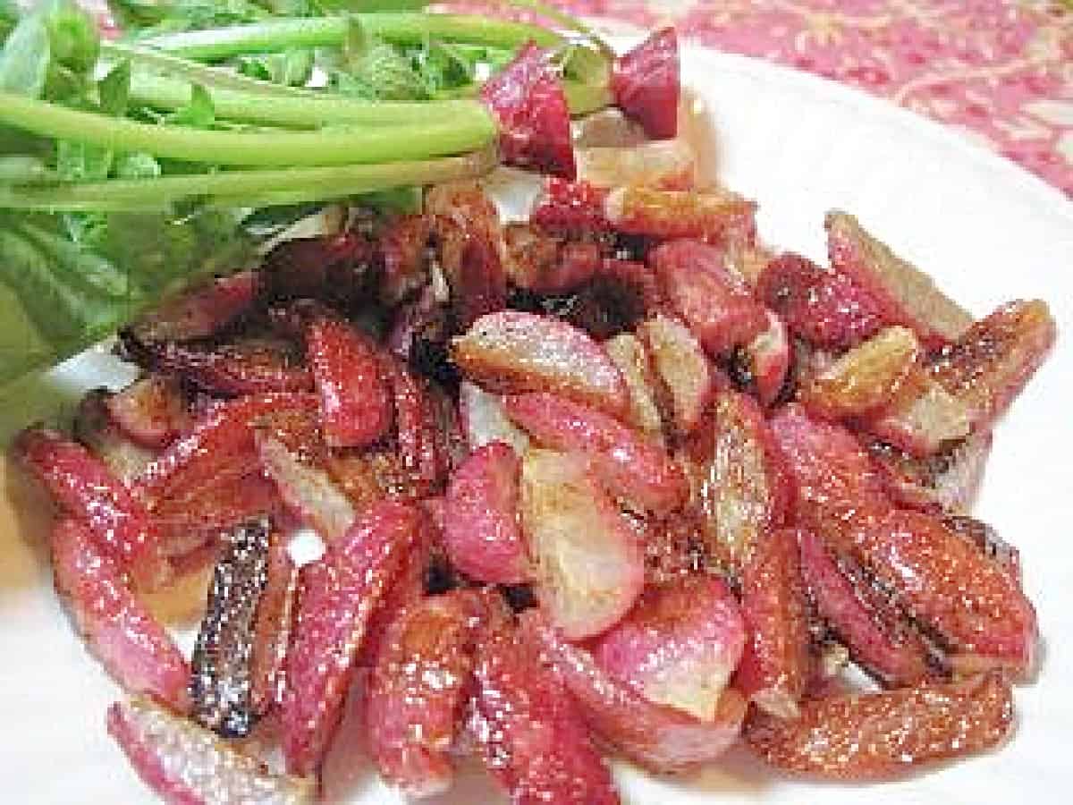 A white plate filled with quartered Roasted Radishes along with some green radish tops on the plate.