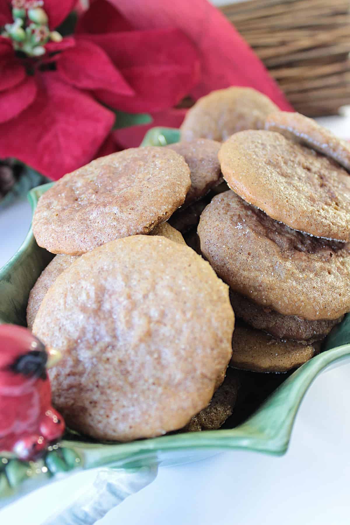 A holly berry Christmas dish filled with Soft Cinnamon Sugar Gingerbread Cookies along with poinsettias in the background.