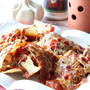 A serving of Pepperoni Pizza Nachos on a white plate with melted cheese and sauce.