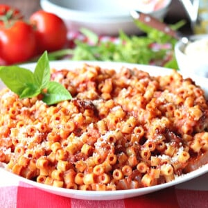 A white bowl filled with Bacon Tomato Pasta with fresh tomatoes and basil in the background.