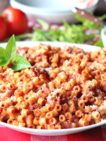 A white bowl filled with Bacon Tomato Pasta with fresh tomatoes and basil in the background.