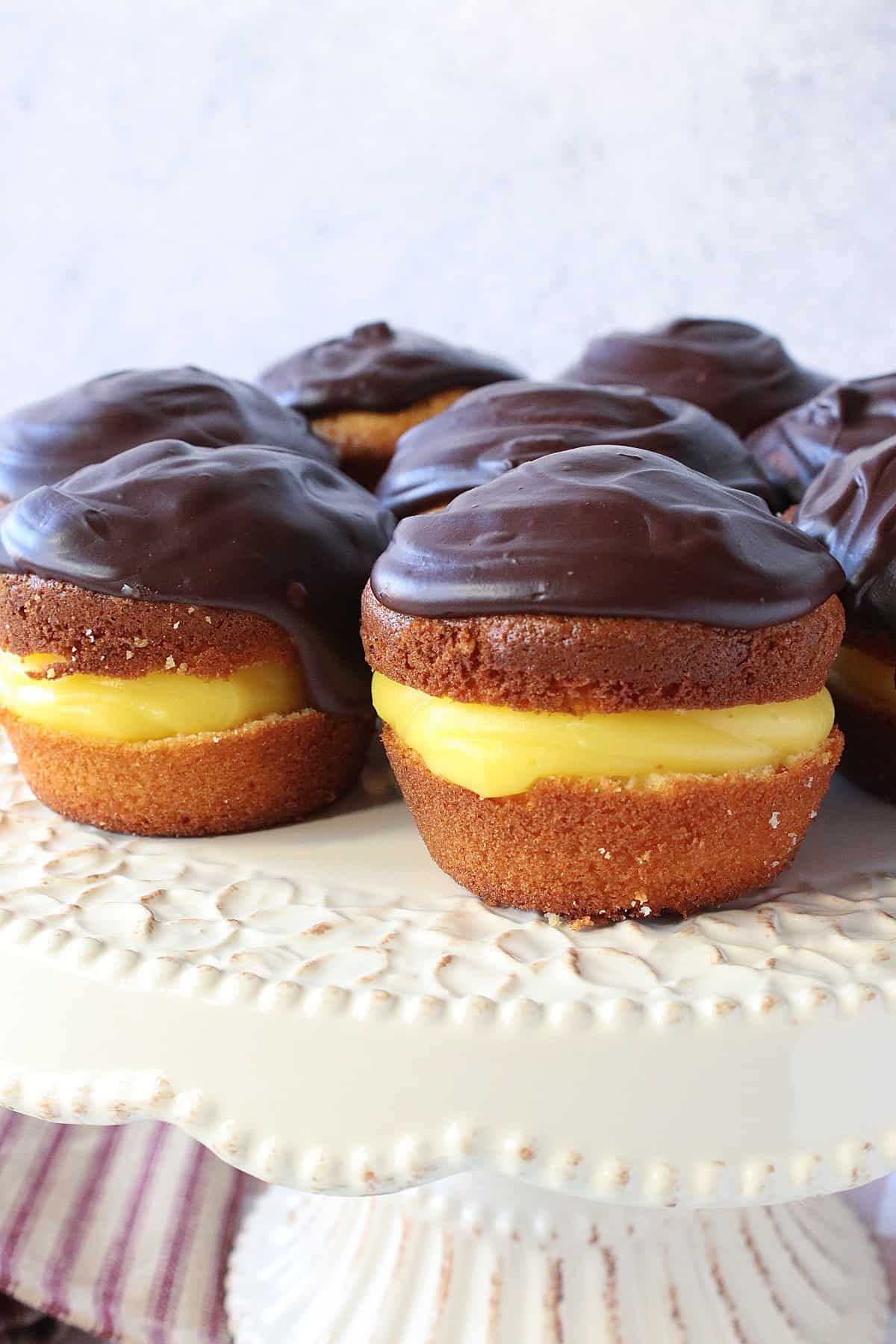 A cake plate filled with Boston Cream Cupcakes with chocolate ganache frosting on top.