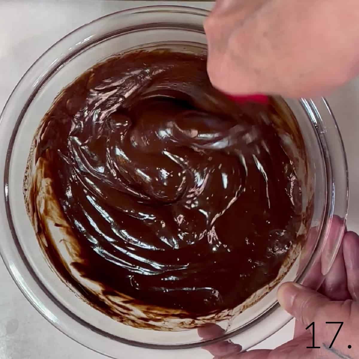 A bowl of glossy brown melted chocolate ganache for Boston Cream Cupcakes.
