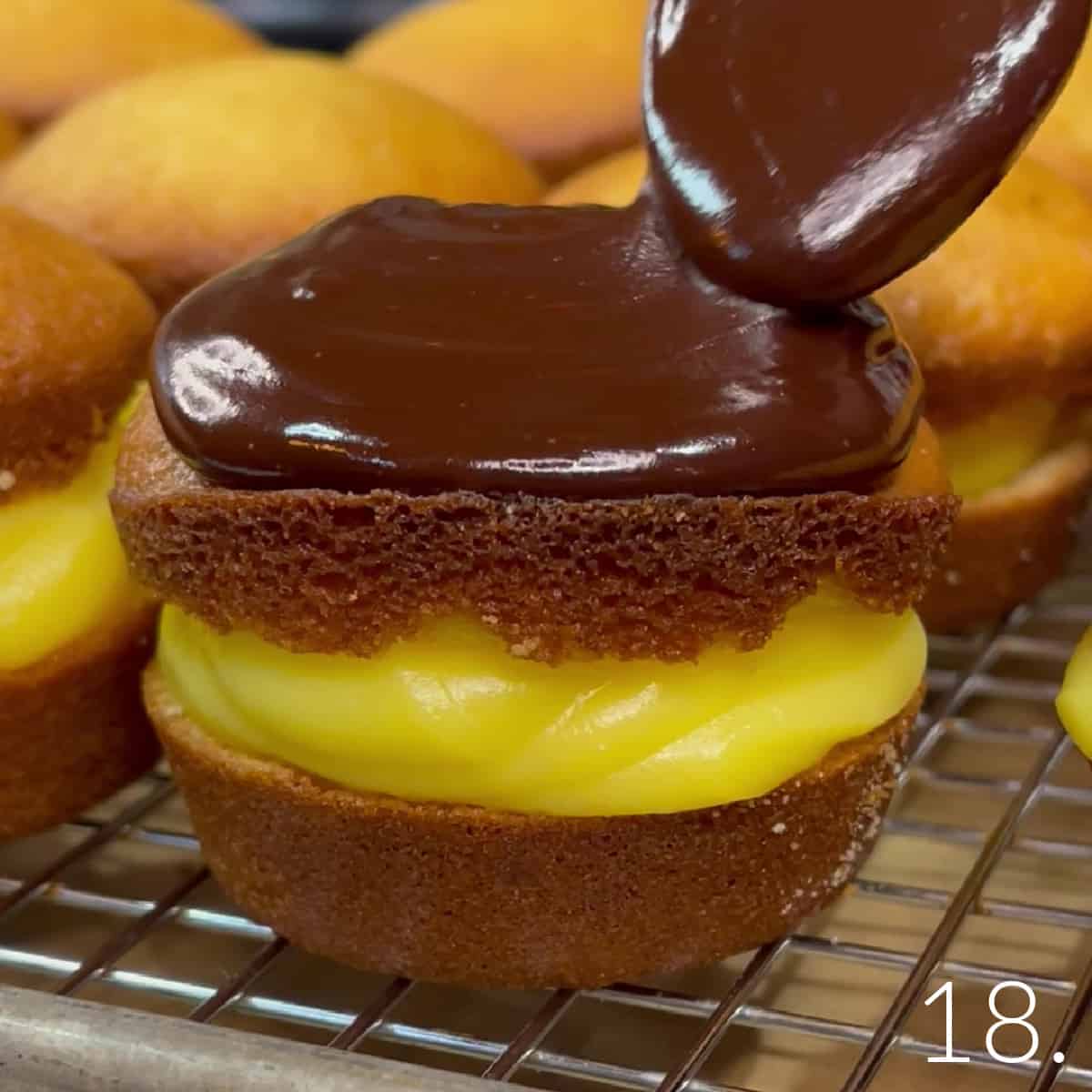A glossy chocolate ganache frosting being put onto a Boston Cream Cupcake with a spoon.