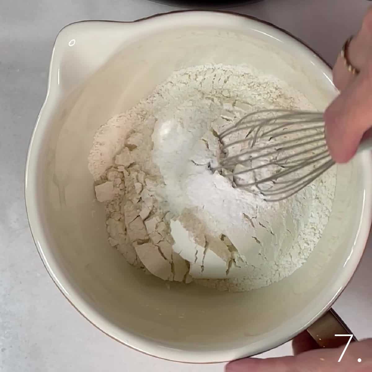 A mixing bowl and a whisk mixing flour, salt, and baking powder.