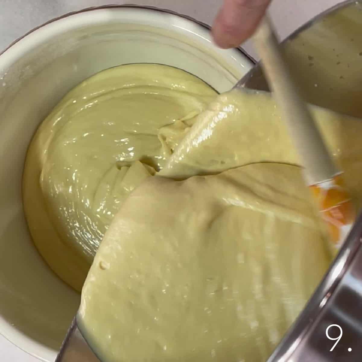 Golden cupcake batter being poured into a bowl with a pour spout.