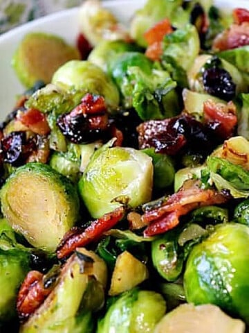 A closeup photo of Sauteed Brussels Sprouts with Candied Bacon and dried cranberries in a bowl.