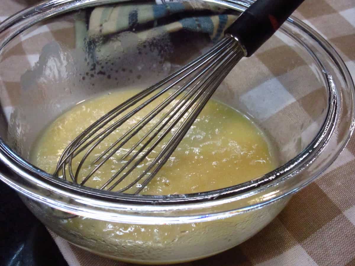 A glass bowl with a whisk along with melted butter and egg white.