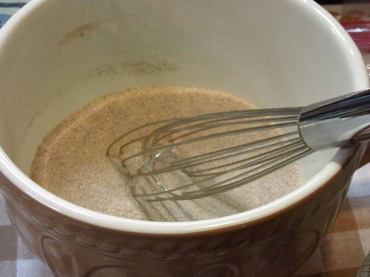 A bowl filled with a mix of cinnamon and sugar along with a whisk.