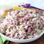 A white bowl filled with Corned Beef and Cabbage Coleslaw with cheese and onion.