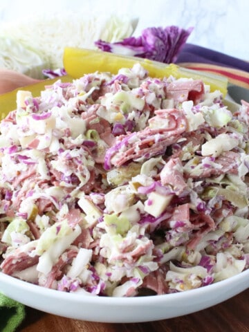 A white bowl filled with Corned Beef and Cabbage Coleslaw with cheese and onion.